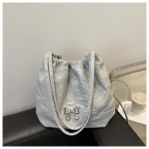 Detail of silver pleated shoulder bag with metallic bow charm on a minimalist leather seat