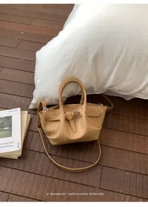 Detail of caramel woven bucket bag with silver buckle and crossbody strap on wood floor
