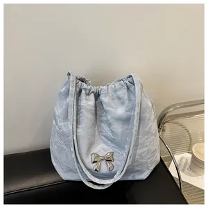 Detail of light blue pleated tote bag with a silver metal bow ornament and drawstring top