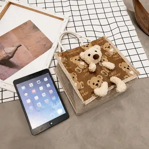 Size comparison of a brown canvas bear lunch bag with a tablet on a checkered background