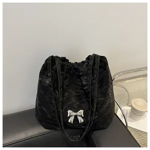 Detail of black glossy pleated shoulder bag with a silver metal bow accent for women