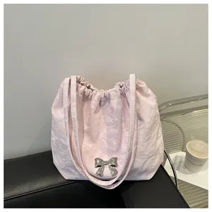 Detail of light pink pleated tote bag featuring a metallic silver bow on a black sofa