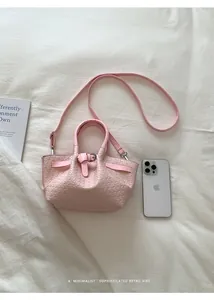 Pink woven bucket bag shown next to a smartphone for size reference in a clean setting
