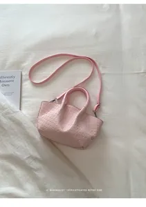 Detail of light pink woven bucket bag with dual handles and slim shoulder strap