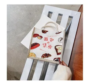 Detail of cream canvas tote bag featuring Japanese bread illustrations on a wood bench