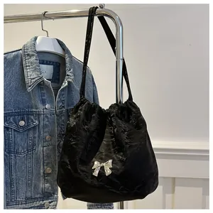 Detail of black pleated satin bucket bag featuring a silver metal bow and shoulder strap