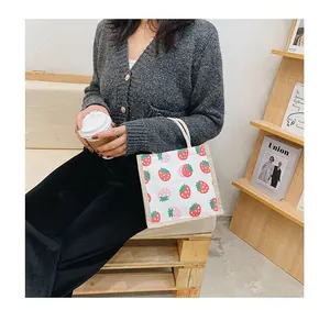 Detail shot of a canvas tote bag with strawberry prints held in a cozy cafe setting