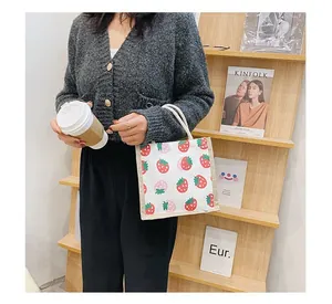 Close-up of a small canvas tote bag with red strawberry print and cotton rope handle