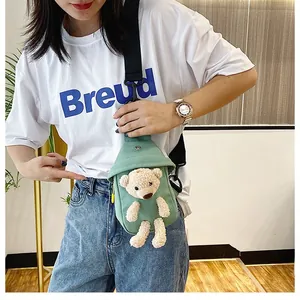 Detail of green canvas crossbody bag featuring a 3D plush bear and adjustable strap