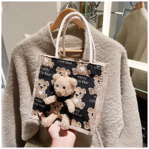 Detail of canvas tote bag featuring bear print and 3D plush bear with white rope handles