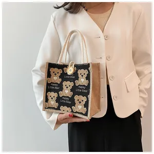 Close-up of a black linen teddy bear tote bag with a woven handle and button closure