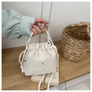 Detail of hand-woven straw bucket bag with floral daisy embroidery and drawstring closure
