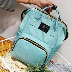 Large mint green diaper backpack with top handle and golden zippers in a white basket