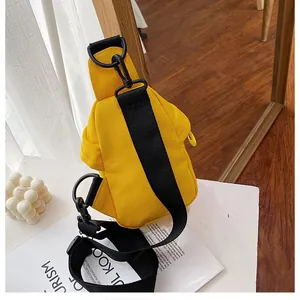 Detail view of a stylish yellow canvas chest bag with black adjustable strap on a white table