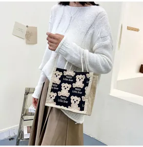Close-up of linen handbag with Happy Little Bear print held by woman in casual outfit