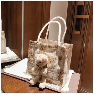Close-up of beige canvas lunch tote with teddy bear print and 3D plush bear charm