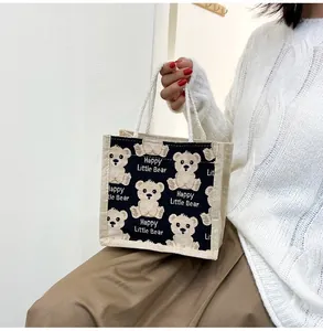 Close-up of linen tote bag with happy little bear print held by a model in casual wear
