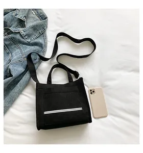 Close-up of black canvas tote bag with white stripe pocket on a white bed sheet
