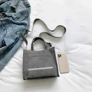 Grey corduroy tote bag with white reflective straps and adjustable shoulder strap on white sheets