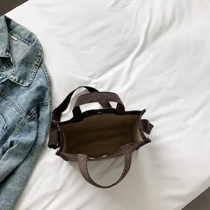 Deep brown corduroy tote bag with adjustable strap and magnetic closure on white cloth