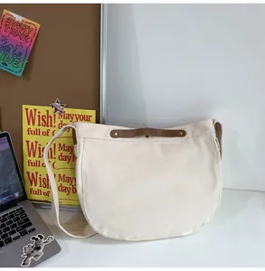 Detail of a cream canvas shoulder bag with brown leather handle and gold rivet accents