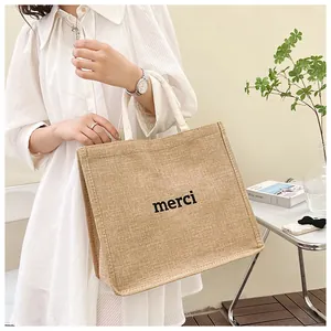 Gros plan sur un sac cabas beige tissé avec inscription Merci porté par un mannequin