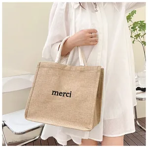 Détail d'un sac cabas en jute naturelle avec imprimé merci et anses en sangle blanche