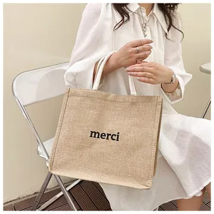Détail du sac cabas en lin avec imprimé merci tenu par un mannequin en robe blanche