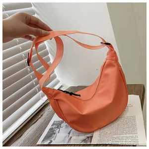 Vista detallada de un bolso bandolera de nailon naranja en forma de media luna con correa