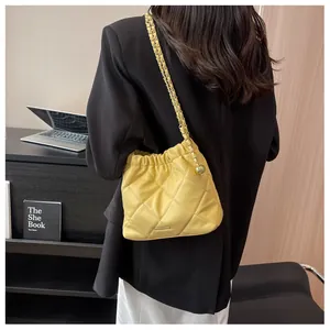 Detail of yellow quilted chain bucket bag with gold ball accent on a black blazer