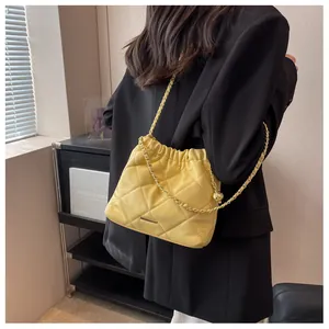 Detail of yellow quilted leather bucket bag with gold chain strap worn on shoulder