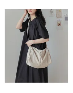 Détail d'un grand sac bandoulière beige en toile souple porté par un mannequin en noir