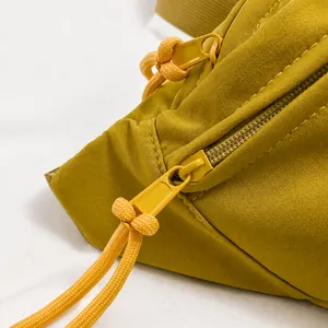 Macro detail of smooth double metal zippers and woven cords on a yellow nylon chest bag