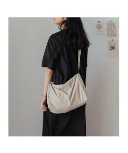 Détail du sac à bandoulière en toile beige plissée porté par un mannequin