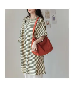 Détail d'un grand sac bandoulière en nylon orange avec une robe t-shirt à rayures