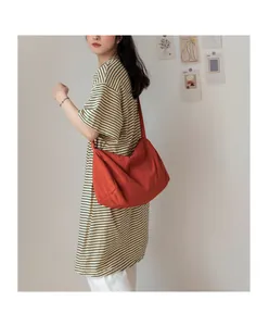 Mannequin portant un grand sac bandoulière en toile rouge orangé montrant sa capacité