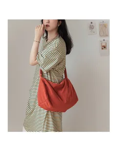 Détail du grand sac bandoulière orange en toile plissée porté par un mannequin en rayures
