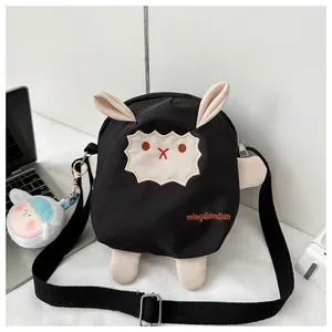 Détail du sac bandoulière mouton noir avec breloque en peluche sur un bureau