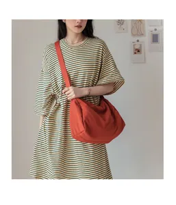 Détail du grand sac bandoulière en toile orange avec texture plissée sur modèle