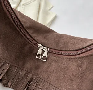 Detailed shot of a dark brown suede crossbody bag with smooth dual zippers and long tassels