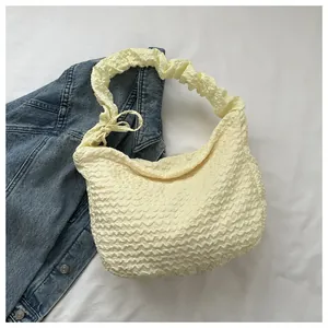 Gros plan du sac en croissant beige en tissu plissé avec détail de nœud sur fond en jean