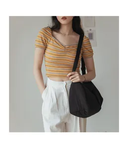 Détail d'un grand sac bandoulière en toile noire porté avec un haut en maille rayé chic
