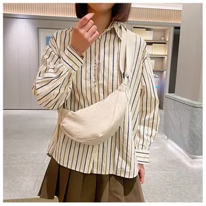 Detail van de crèmekleurige nylon crossbodytas met verstelbare riem gedragen door model