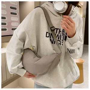 Detail van grijsbruine nylon halve maan crossbodytas met verstelbare riem over een hoodie