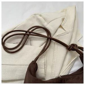 Detail of dark brown suede crescent bag featuring knotted rope strap and metal zipper