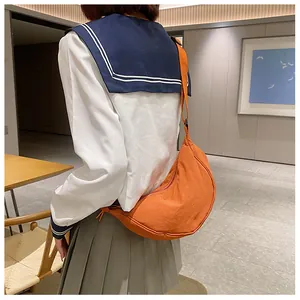 Oranje nylon halve maan crossbodytas gedragen door een model in een binnenruimte