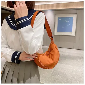 Model met oranje nylon halve maan schoudertas in een minimalistische binnenruimte