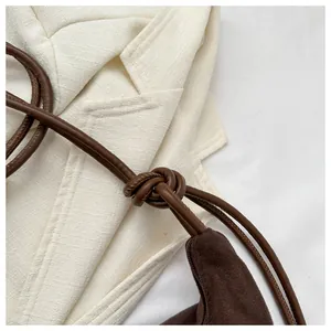 Close-up of dark brown suede crossbody bag with decorative leather knot and strap detail