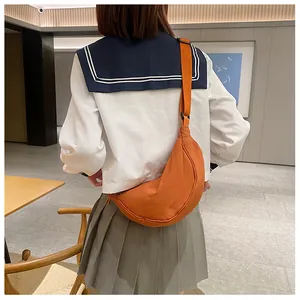 Detail van een oranje nylon halve maan crossbodytas gedragen door een casual model