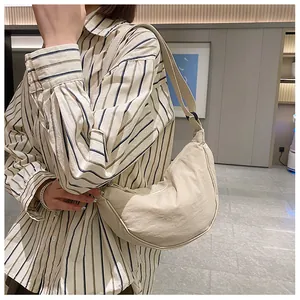 Zijaanzicht van een beige halve maan crossbodytas op een model in een kamer